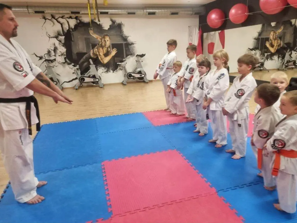 Zdjęcie WhatsApp 2024-11-08 o 11.08.09_a999f9b4 Instruktor karate prowadzi zajęcia z dziećmi na macie.